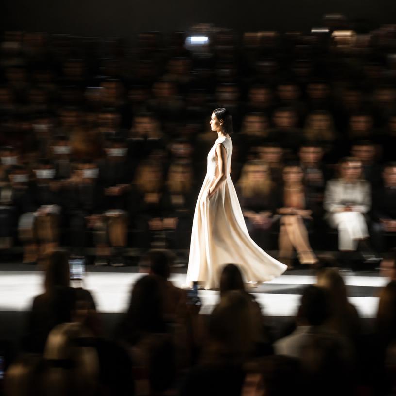 Runway show crowd in blurred motion with a single lit figure walking
